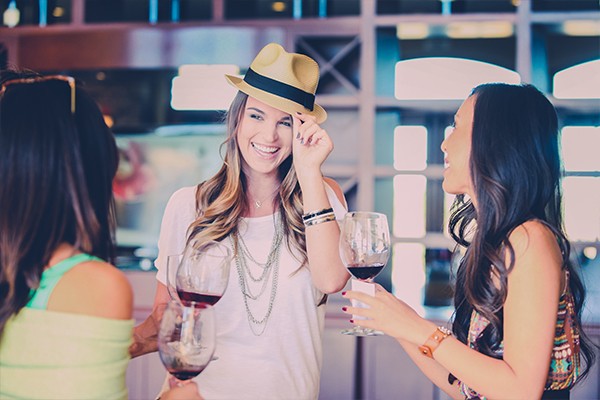 Girl with hat and friends tasting red wine