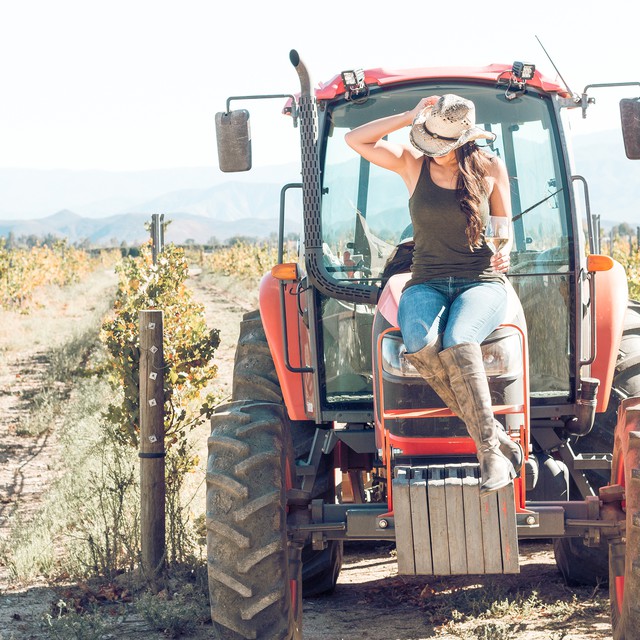 Girl in cowgirl boots holding glass of white wine from Ponte Vineyards while sitting on a tractor in Temecula Valley Wine Country