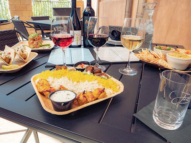 An outdoor picnic table setup with a variety of wines and paired lunch items