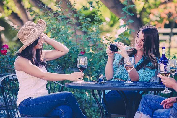 Girlfriend taking picture of girl with red wine