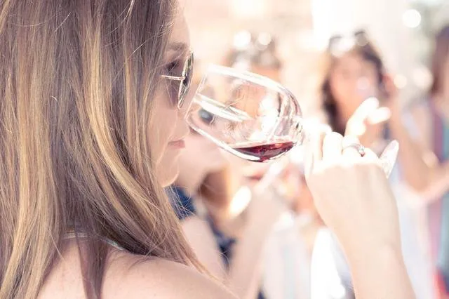 A young woman smells her white wine before tasting it