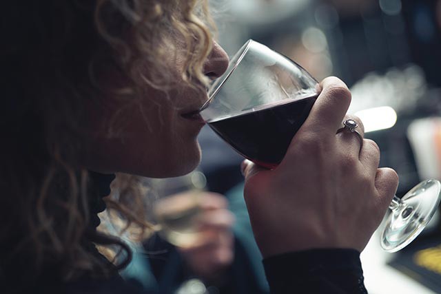 Girl smells glass of red wine before tasting