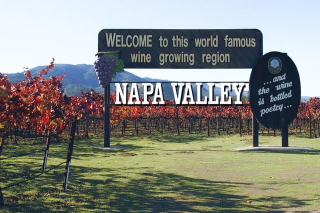 A sign welcoming guests to Napa Valley with vineyards behind it