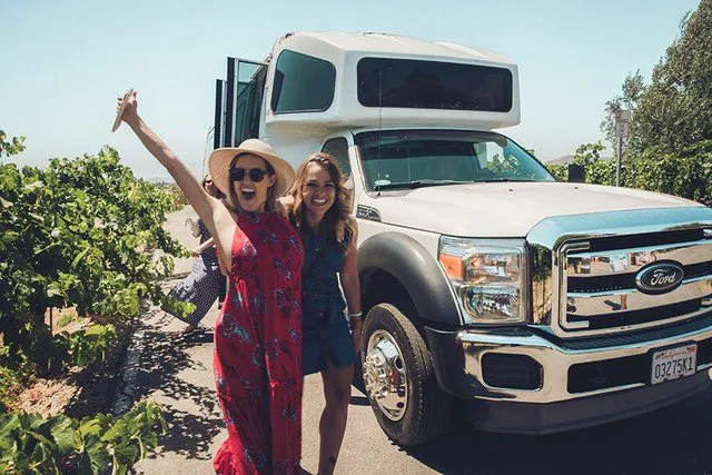 Girlfriends joyfully heading to winery with Grapeline shuttle in background