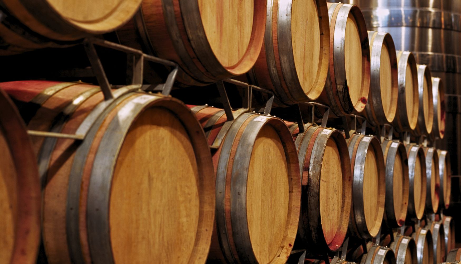 Close-up of stacked wooden wine barrels in a winery storage area, arranged in neat rows.